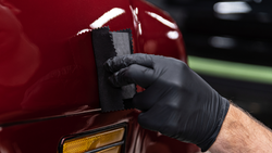 Gloved hand applying car paint glazing product with foam applicator pad