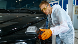 Professional detailer checks black vehicle paint closely for scratches and swirl marks